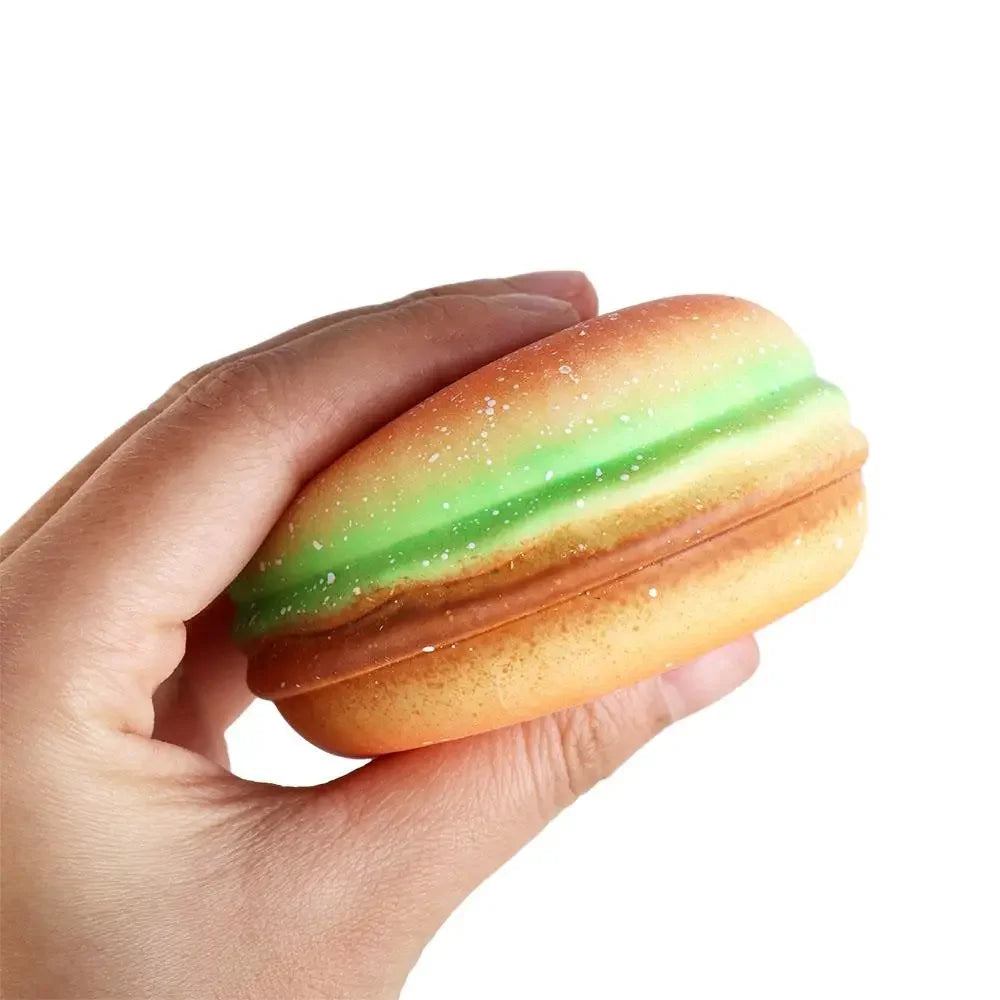 A hand holds an adorable, squishy sensory toy shaped like a burger with green and orange layers.