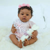 A baby doll named Abigail with soft body is shown wearing a pink dress and a floral headband, sitting on white fur.