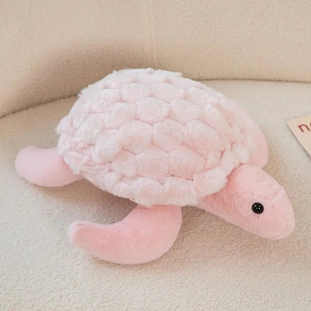 A soft pink sea turtle plush toy with a textured shell and small black eyes resting on a light surface.