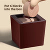 A hand is putting six wooden blocks into a dark brown box for a puzzle challenge.