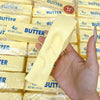 A hand holds a yellow butter squishy stress relief toy packaged in clear plastic.