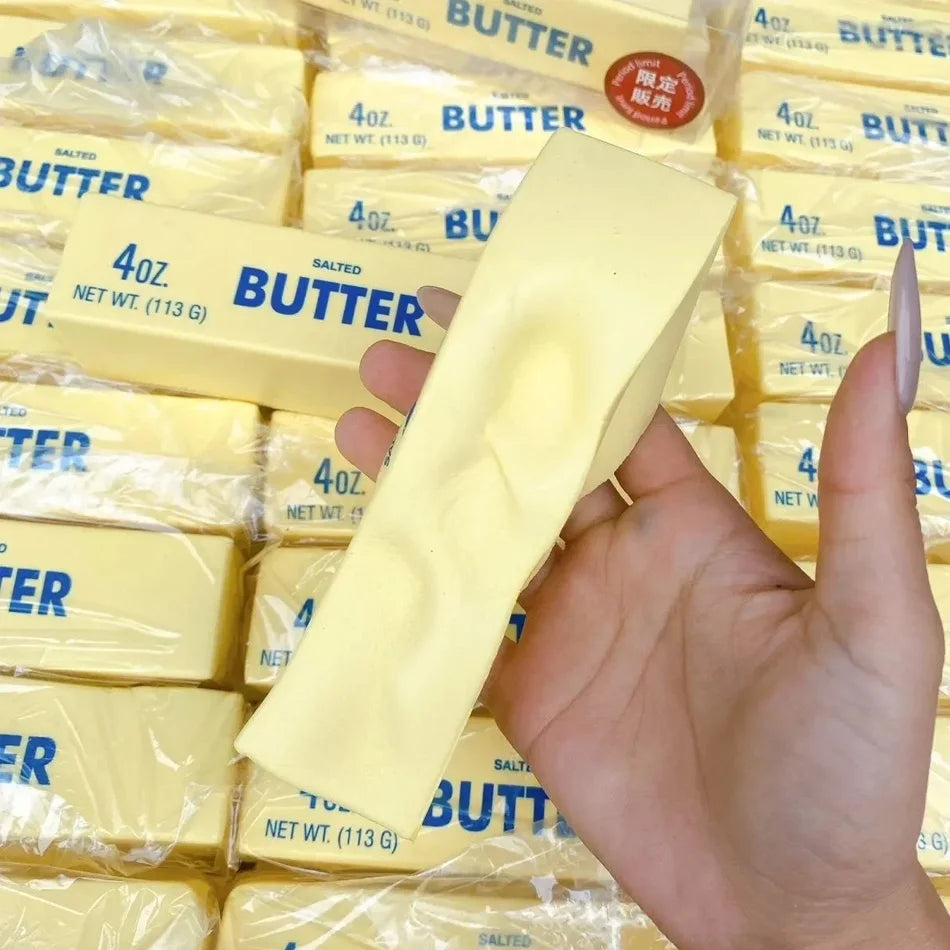 A hand holds a yellow butter squishy stress relief toy packaged in clear plastic.