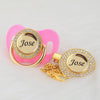 A pink pacifier clip set featuring a gold-toned ring and a crystal charm engraved with the name Jose