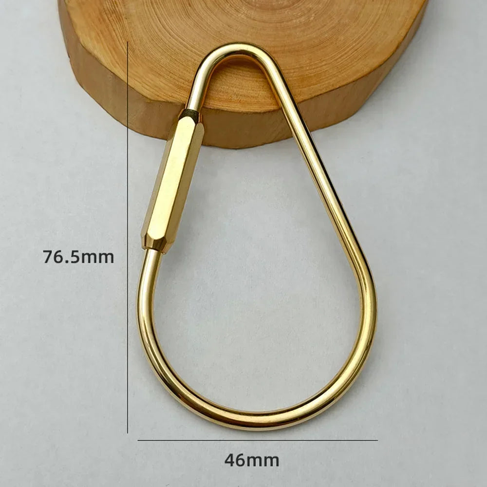 A brass keychain with a locking carabiner clip is shown resting on a wooden surface.