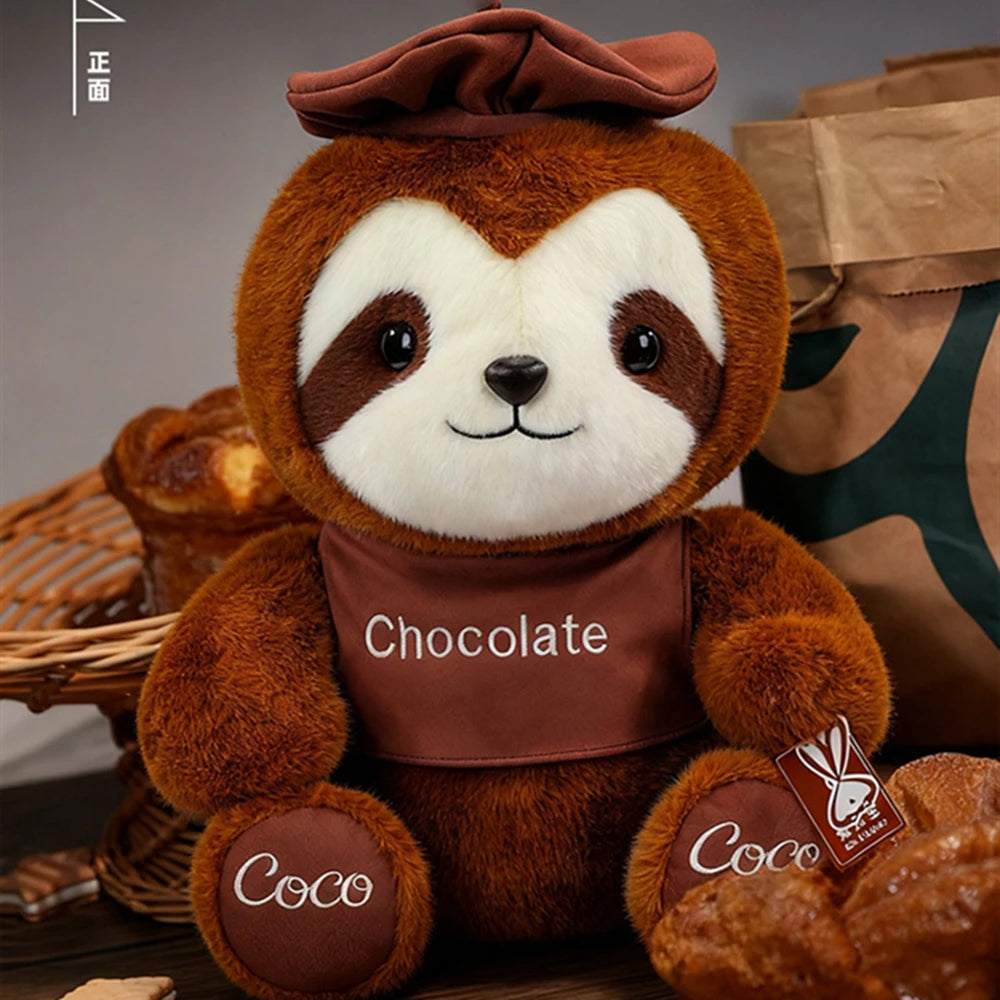 A brown sloth plush toy with white markings and a chocolate-colored chest, sitting on a wooden surface.