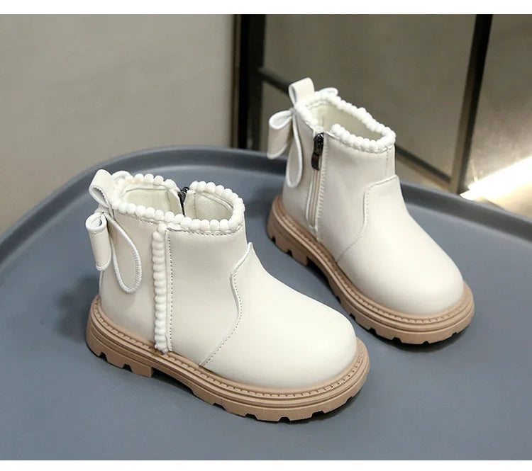 A pair of white cozy kids winter boots with faux leather finish resting on a gray surface.