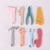 A set of silicone baby teether toys shaped like various tools, including a pink shovel, beige key, green pliers, yellow knife