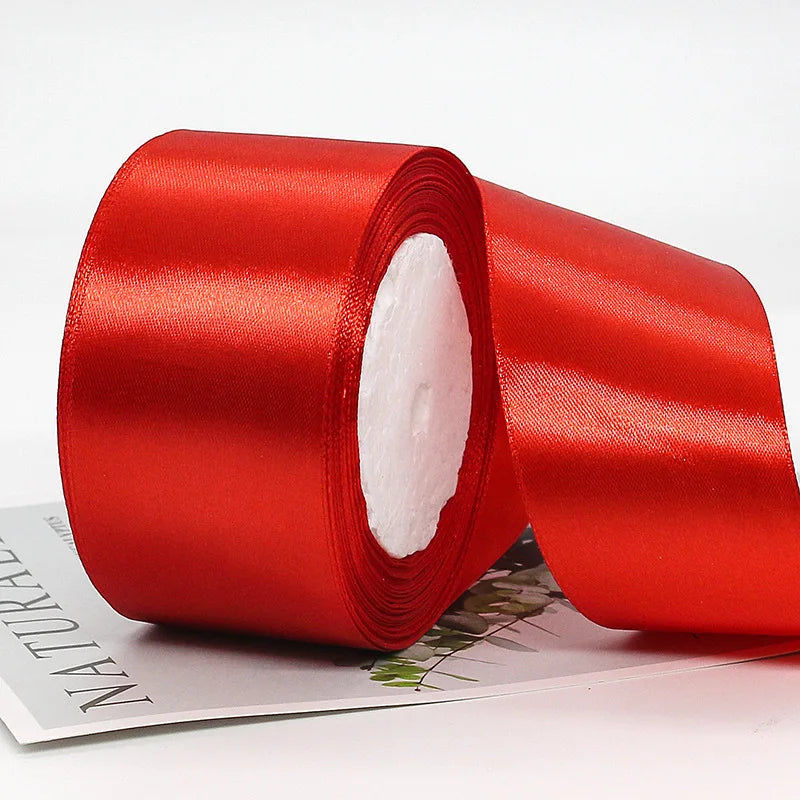 A roll of red satin ribbon used for gift wrapping or crafts, shown lying on a sheet of paper.
