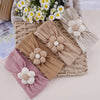 A collection of floral elastic baby headbands in beige, pink, and cream are displayed in a woven basket.