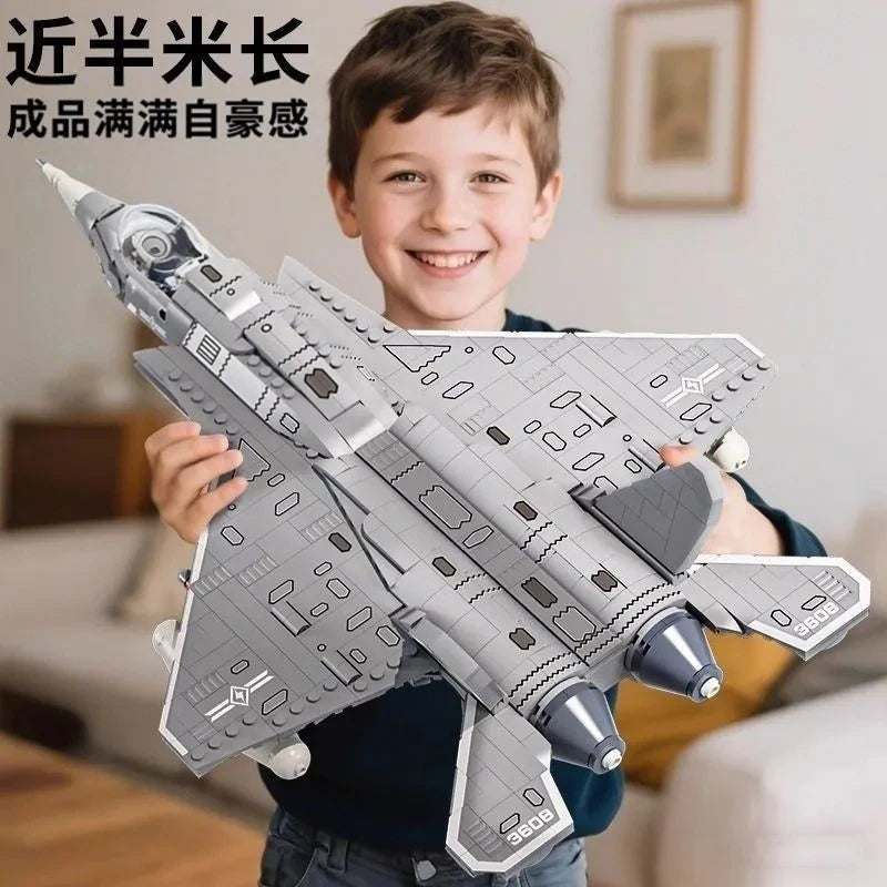 A smiling boy holds a detailed gray fighter jet model kit built from building blocks.