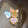 A small, fluffy brown Monchhichi plush toy is shown against a light brown leather background with a measuring scale.