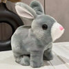 A gray and white plush rabbit toy with large ears sitting on a white surface.