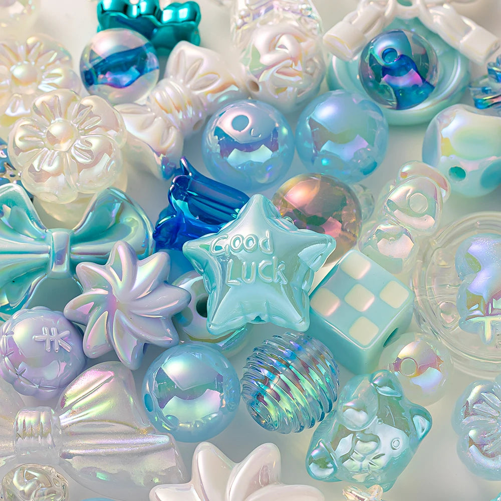A close-up of various iridescent blue and purple acrylic bow and flower beads for DIY jewelry making.