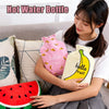 A woman holds a pink and yellow portable hot water bottle with a cozy cover in a living room setting.