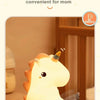 A cute unicorn silicone LED night light is shown illuminating a room, with a hand holding a smartphone remote.
