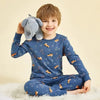 A smiling young boy wearing a blue long-sleeved pajama set with an astronaut print, sitting on a white fluffy surface.