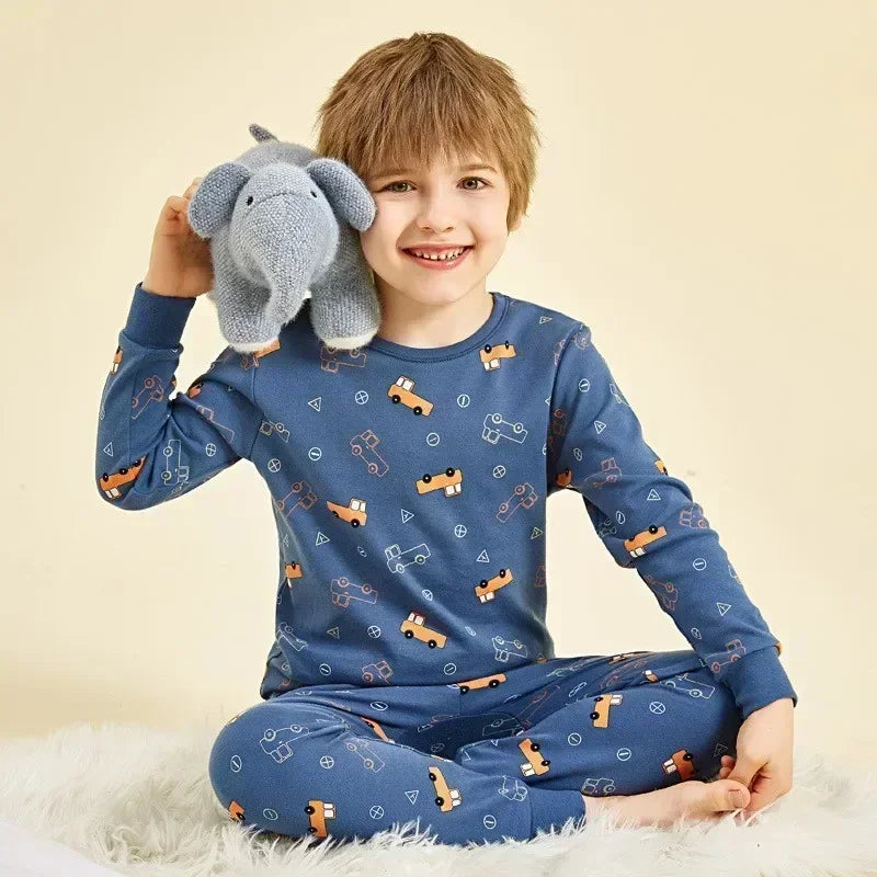 A smiling young boy wearing a blue long-sleeved pajama set with an astronaut print, sitting on a white fluffy surface.