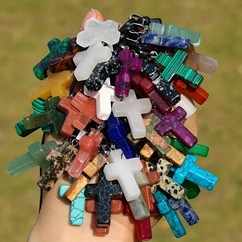 A collection of natural stone cross pendants in various colors and shapes held in a hand.