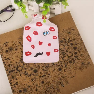 A pink portable hot water bottle with a cozy cover featuring red lips and hearts, resting on brown patterned fabric.