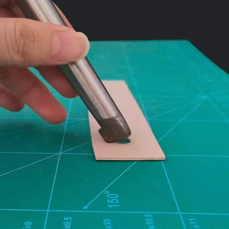 A hand is using a metal punch tool to create a hole in a piece of light pink leather for crafting.