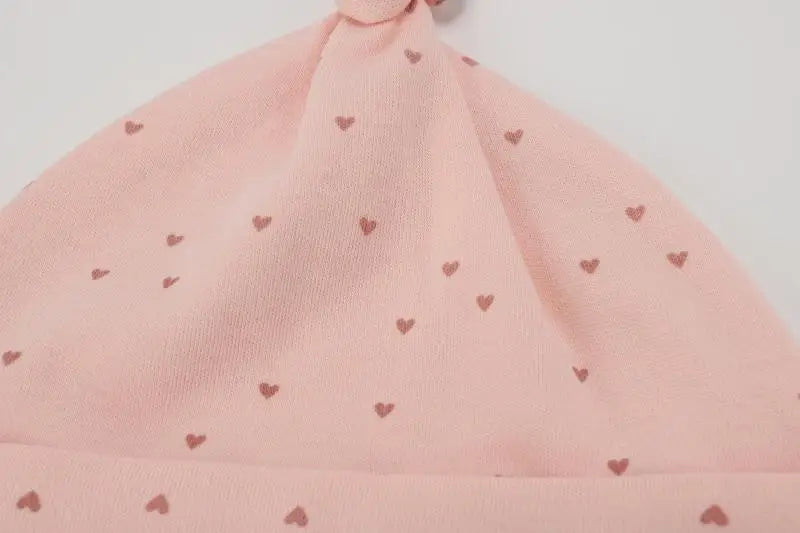A light pink knitted baby hat with small heart embroidery on the crown and brim.