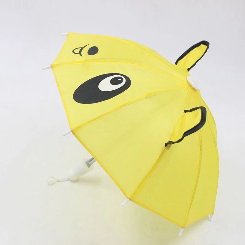 A yellow umbrella shaped like a bear face with black eyes and features, used as a mini doll accessory.