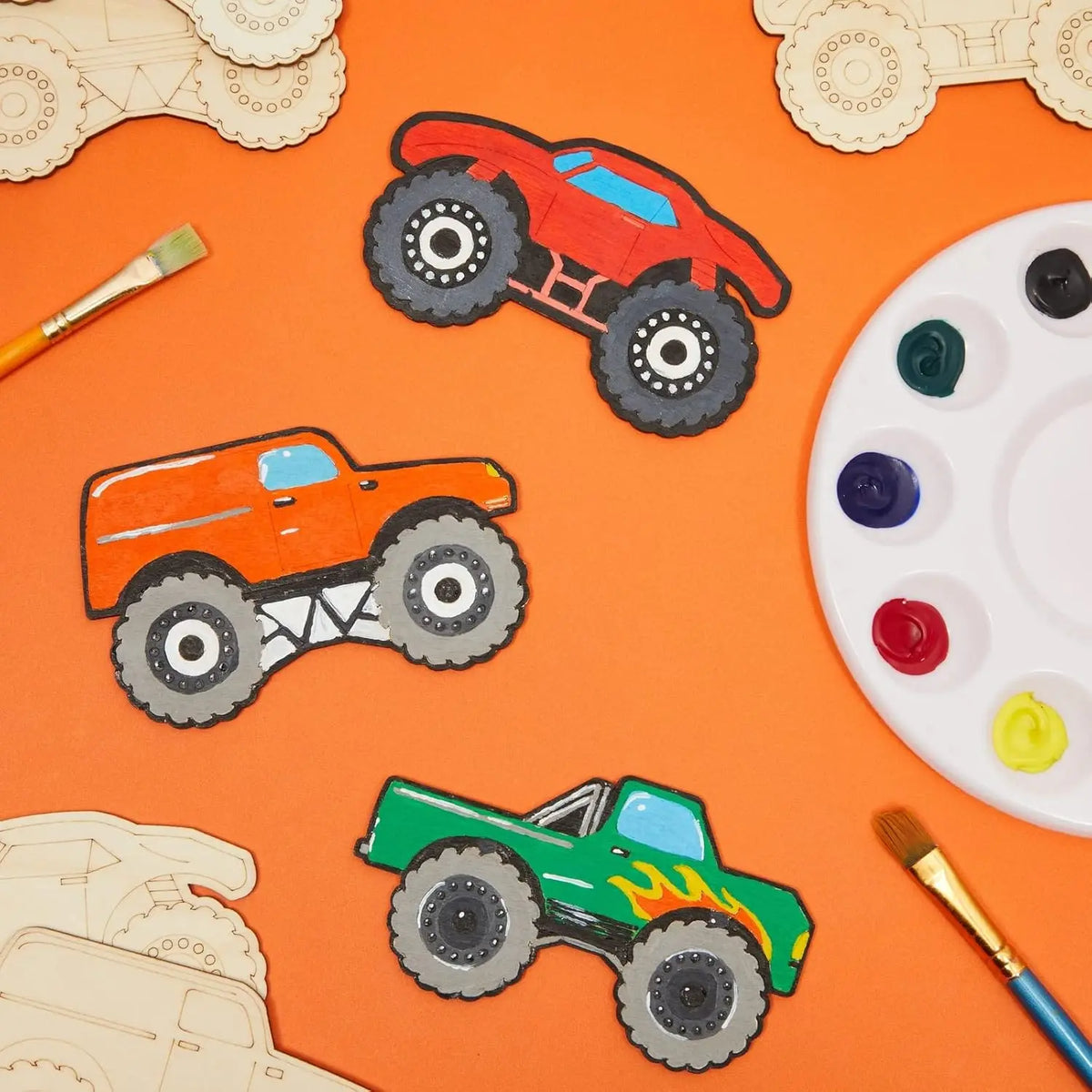 A collection of unfinished wood monster truck cutouts in various colors and sizes laid on an orange background.