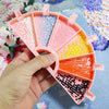 A hand holds a pink diamond painting organizer tray divided into six compartments filled with various colored sequins and bea