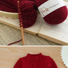 A red knitted sweater and yarn balls are displayed on a wooden surface.