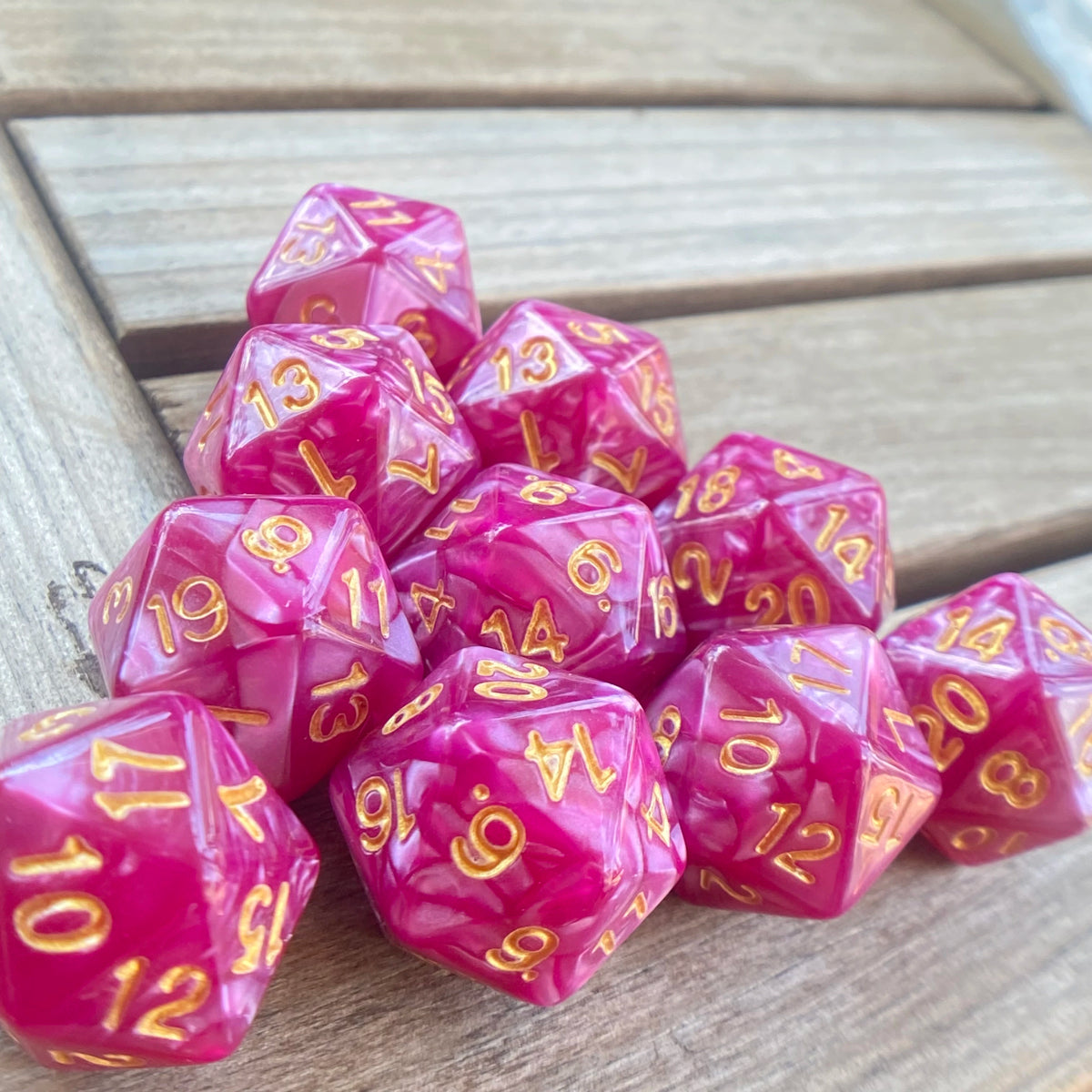 A collection of ten pink and purple pearl acrylic D20 dice scattered on a wooden surface.