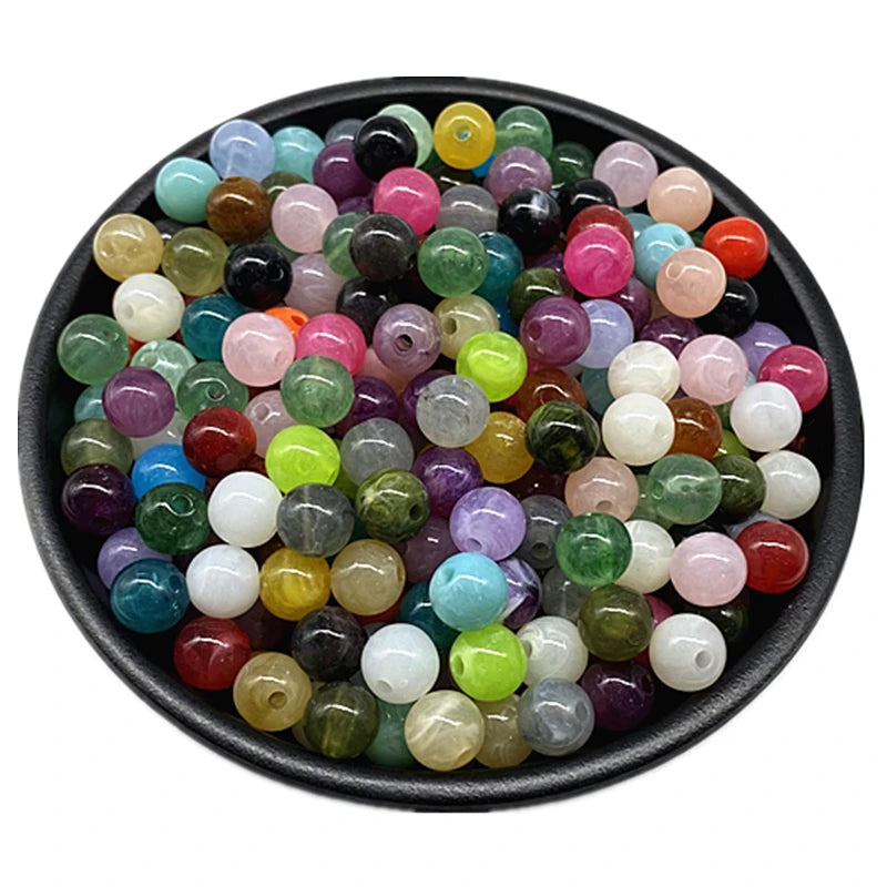 A collection of colorful acrylic round beads in various shades of green, pink, purple, and yellow are displayed in a black bo