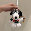 A white Snoopy plush toy wearing a red and green patterned scarf and black sunglasses is being attached to a white string.