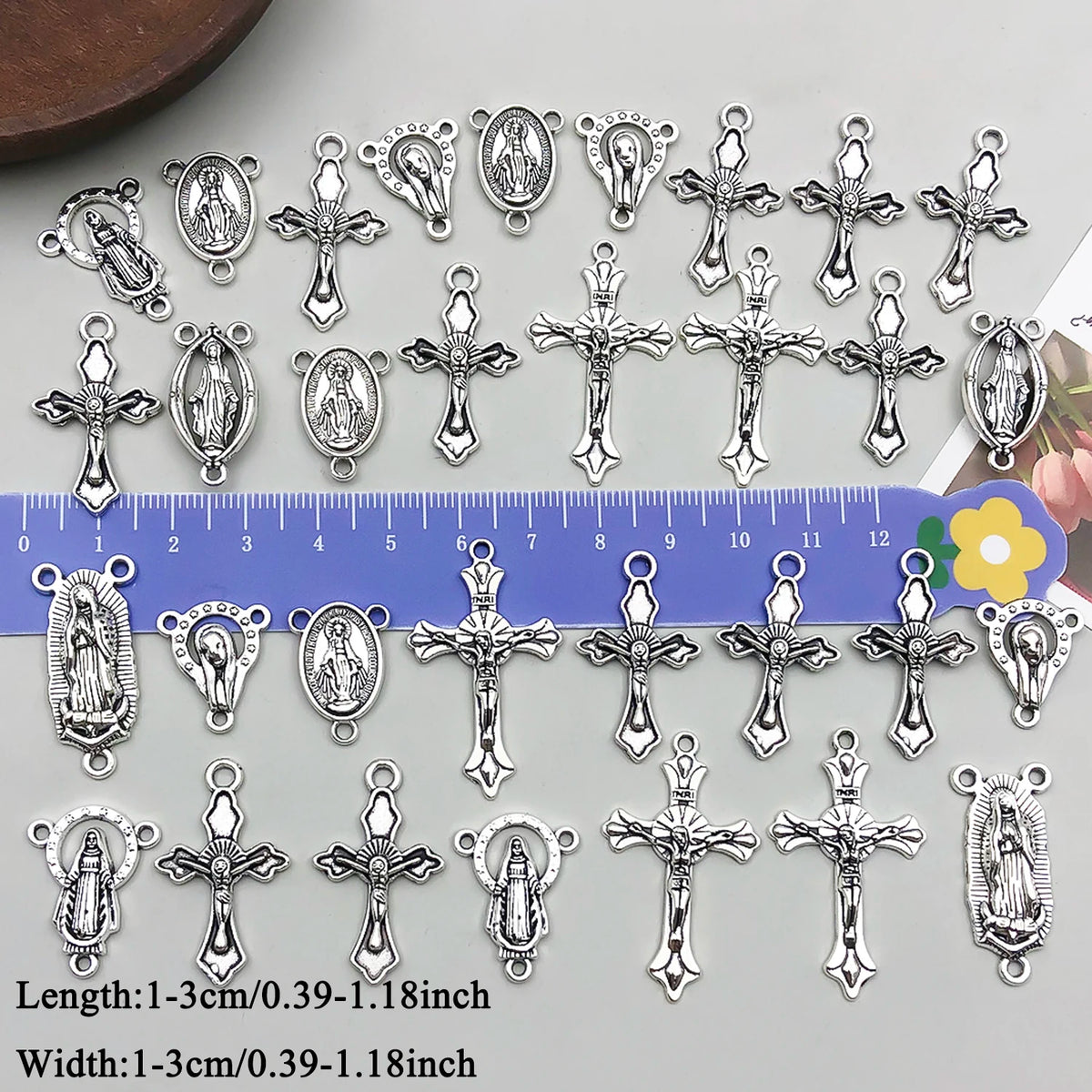 A collection of vintage antique silver cross charms and pendants for jewelry making displayed on a ruler.