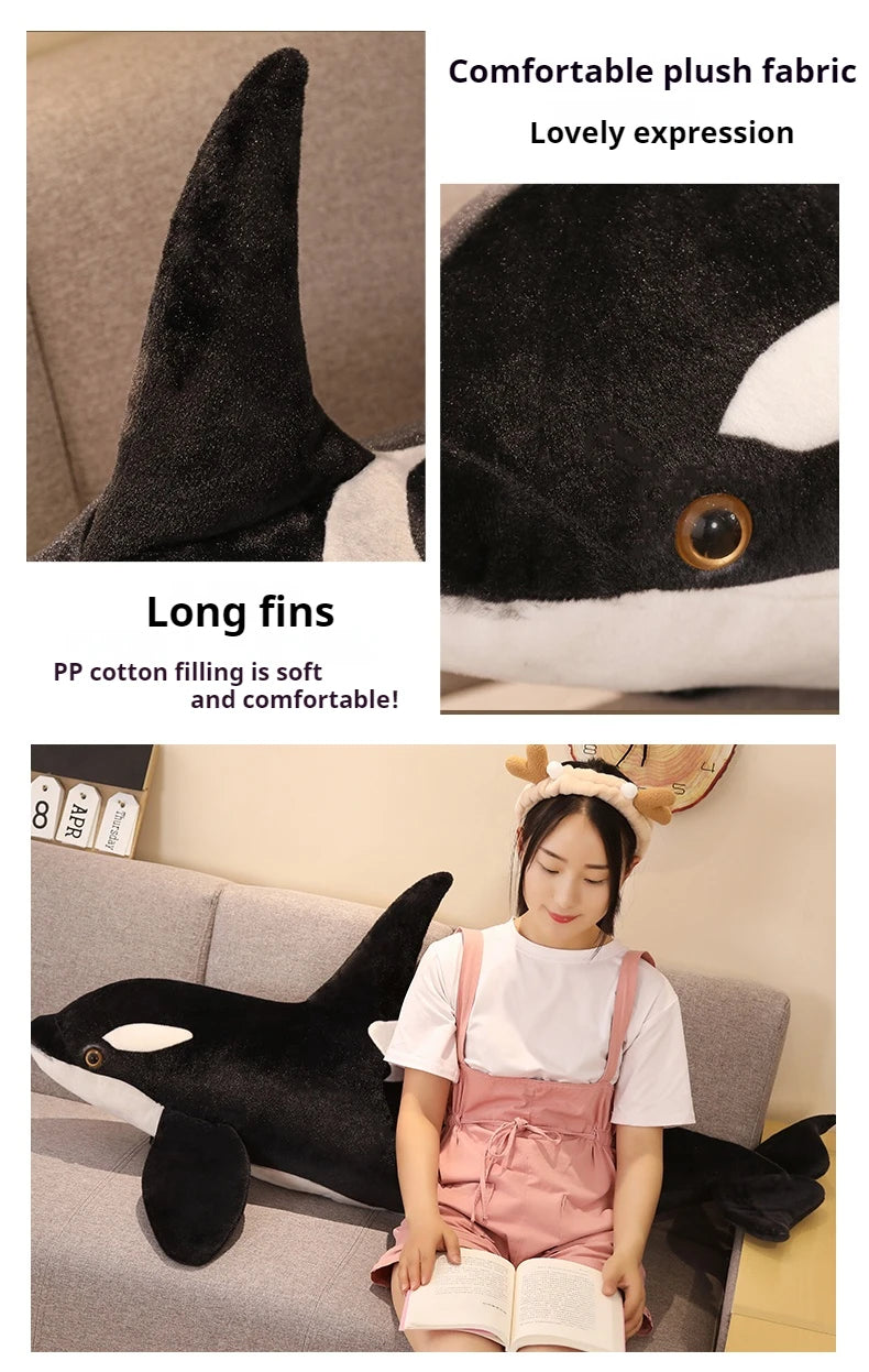 A black and white lifelike orca whale plush toy with long fins is shown next to a person reading a book.