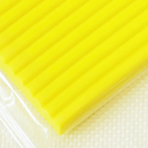 A close-up of a bright yellow block of soft modeling clay with ribbed texture.
