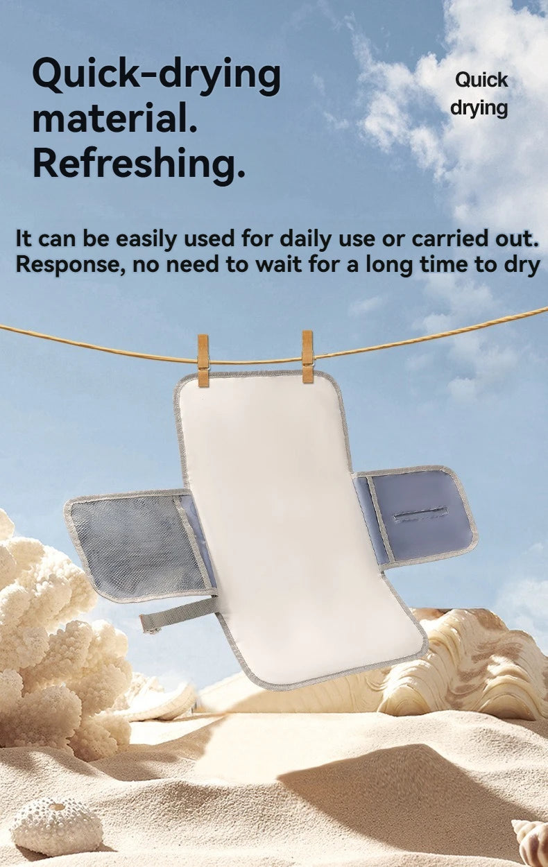 A white portable waterproof baby changing mat with a blue carry handle is shown hanging on a line against a cloudy sky.