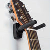 A brown acoustic guitar is mounted on a black wall hanger with tuning pegs visible.