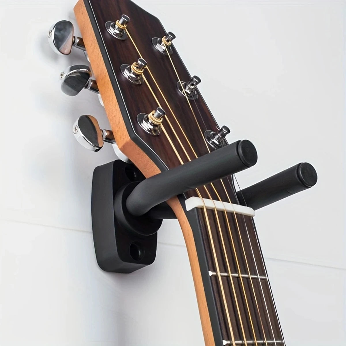 A brown acoustic guitar is mounted on a black wall hanger with tuning pegs visible.