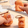 An orange capybara pinch toy is shown being held by a hand, with another version resting nearby.