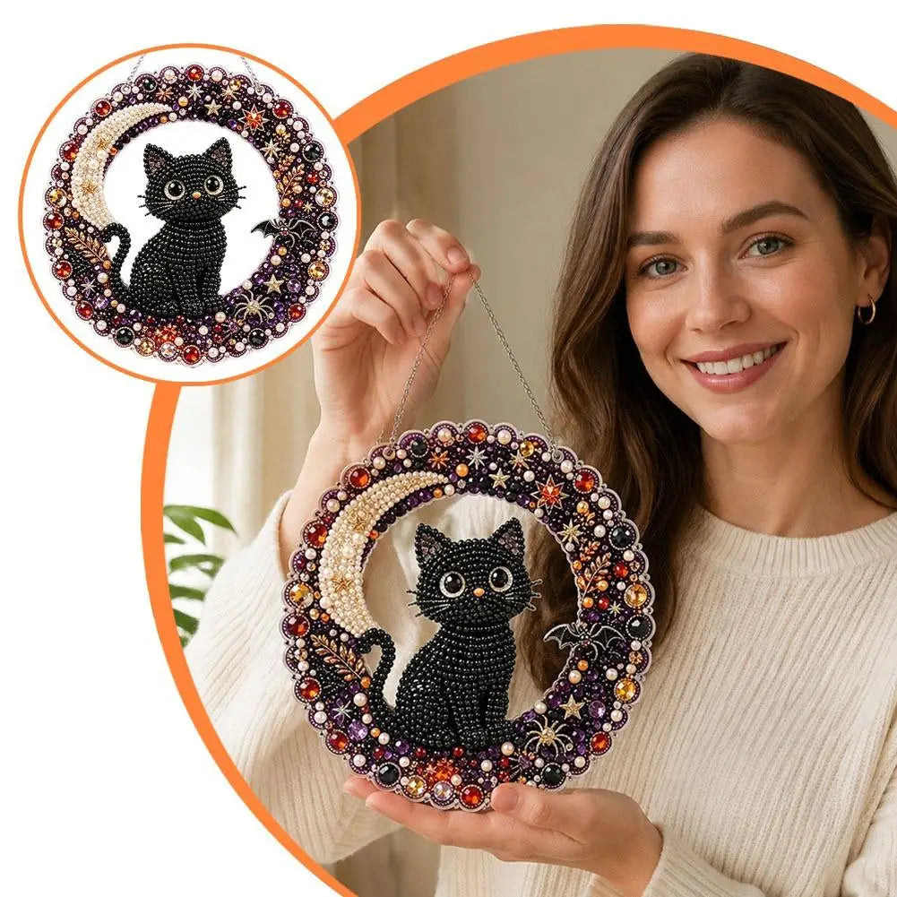 A woman holds a finished Halloween diamond painting hanging ornament kit featuring a black cat surrounded by colorful jewels.