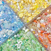 A close-up of various colorful acrylic bow and flower beads in shades of blue, yellow, pink, and green for DIY jewelry making