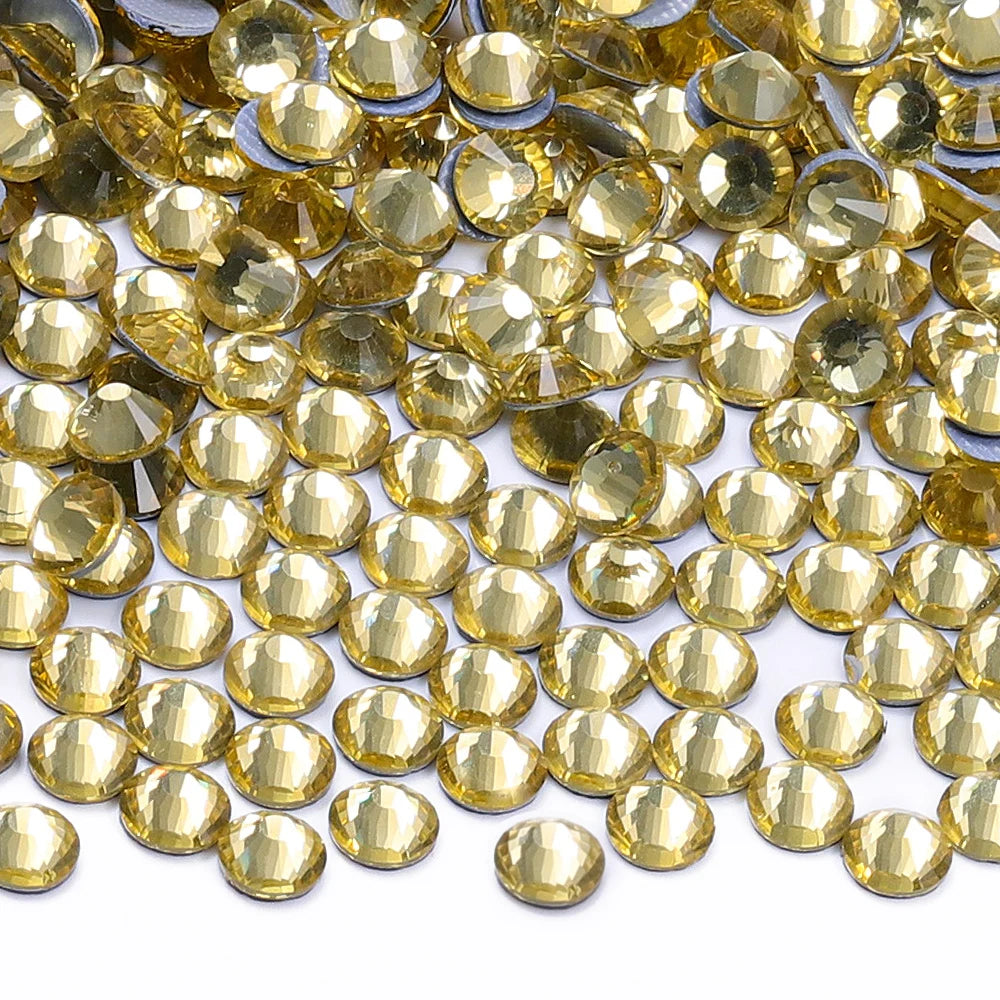 A close-up view of small, round, faceted gold glass crystal rhinestones scattered on a white background.