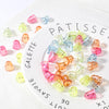 A white plate holds various colored acrylic ghost beads for jewelry making.