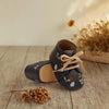 Ein Paar dunkelbrauner Unisex-Sandalen für Säuglinge und Kleinkinder mit Blumenstickerei auf einer Holzoberfläche.
