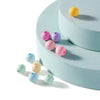A collection of matte acrylic round beads in yellow, pink, purple, and blue resting on a light blue surface.