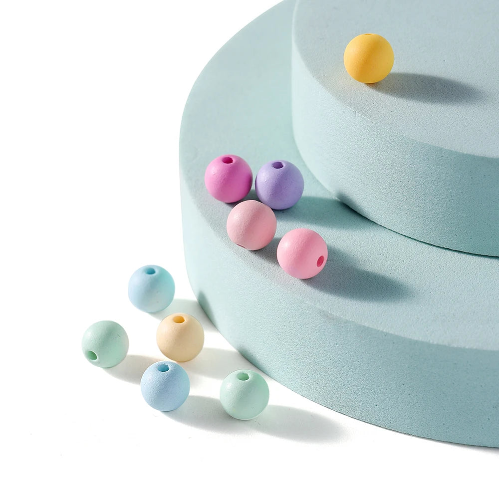 A collection of matte acrylic round beads in yellow, pink, purple, and blue resting on a light blue surface.