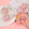 A hand holds several colorful rainbow squishy stress relief balls next to a plate with the words good morning.