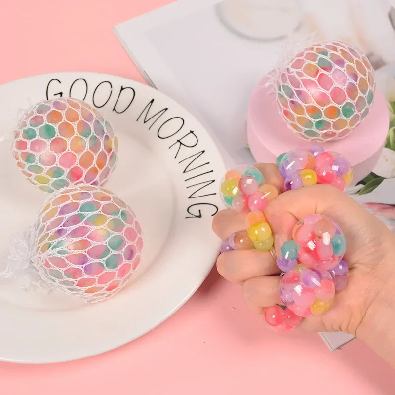 A hand holds several colorful rainbow squishy stress relief balls next to a plate with the words good morning.
