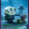 A green Minion collectible figure with large goggles sits next to a small brown bear figure in an outdoor setting.
