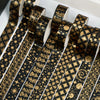 A set of twenty rolls of black and gold foil washi tape, featuring intricate patterns like stars and foliage.